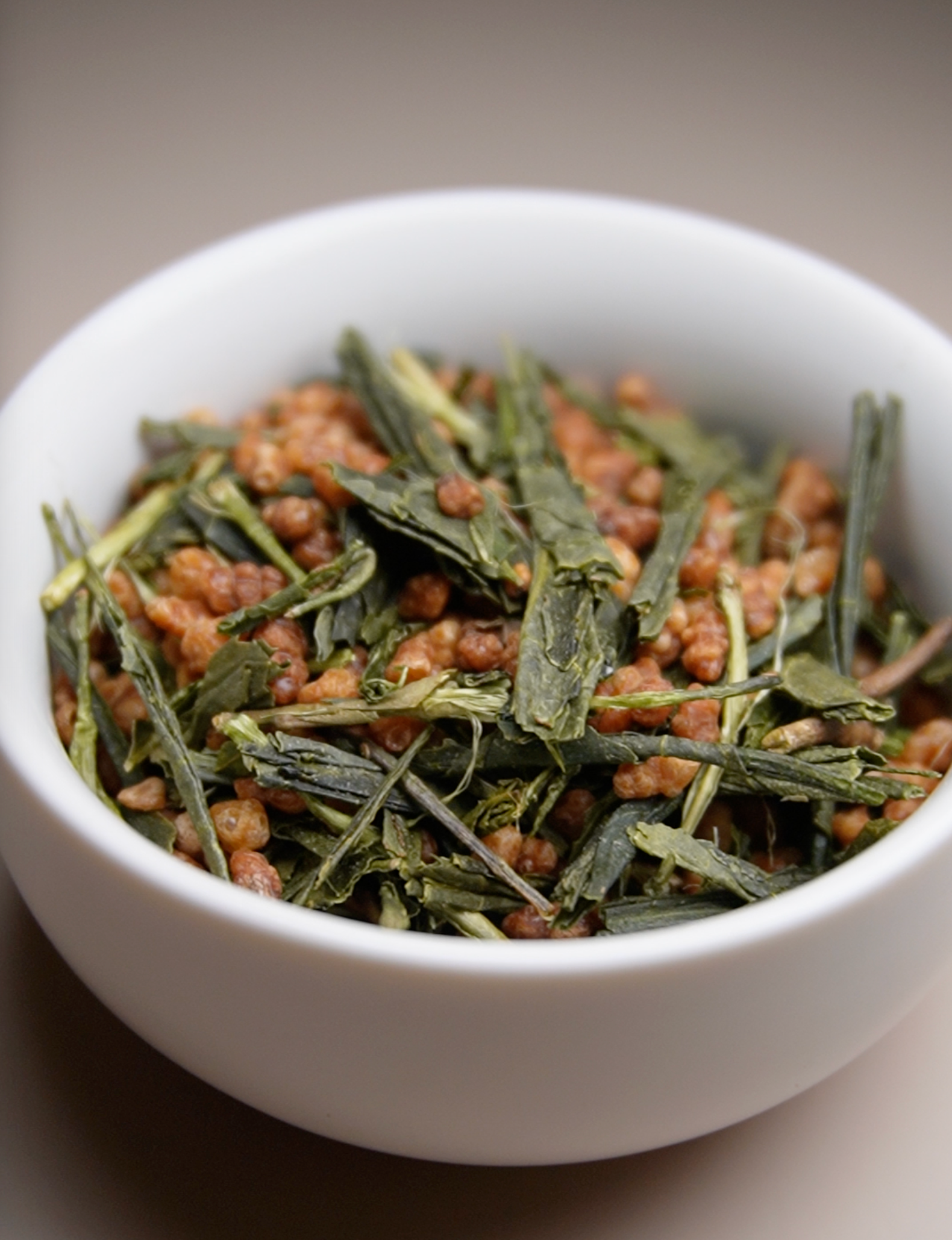 White bowl filled with green tea leaves on a neutral background
